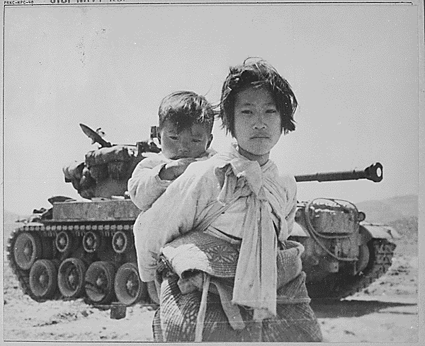 With her brother on her back a war weary Korean girl tiredly trudges by a stalled M-26 tank, at Haengju, Korea., 06/09/1951.  Credit: National Archives