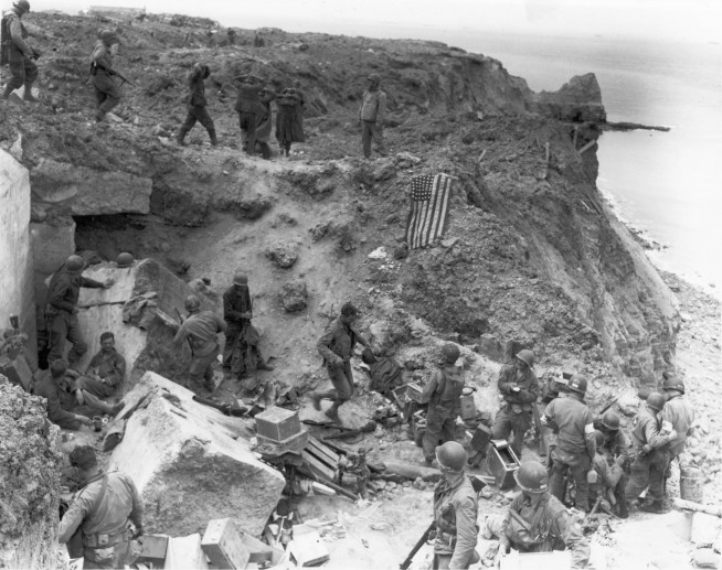 Photo taken on D+2, after relief forces reached the Rangers at Point Du Hoe. The American flag had been spread out to stop fire of friendly tanks coming from inland. Some German prisoners are being moved in after capture by the relieving forces. Image and caption credit: U.S. Army Center of Military history.