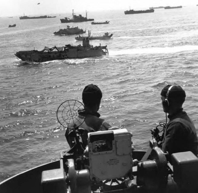 Gun Crew Alert aboard the cruiser USS Augusta, as landing craft approach the coast of France during the invasion, 6 June 1944. The three landing craft nearest the Augusta are an LCT(6), an LBV, and an LBK. While the Allied air forces were bombing installations along the invasion beaches the Allied sea armada drew in toward the coast, preceded by its flotillas of mine sweepers. Bad weather conditions and high seas had driven the enemy surface patrol craft into their harbors, and the 100-mile movement across the English Channel was unopposed. By 0300 the ships had anchored in the transport areas some thirteen miles off their assigned beaches, and the loading of troops into landing craft and the forming of the assault waves for the dash to the beaches began. At 0550 the heavy naval support squadrons began a 45-minute bombardment which quickly silenced the major coast-defense batteries. Image and caption credit: Center of Military History.