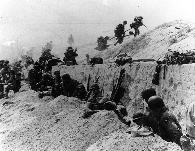 U.S. Soldiers of the 8th Infantry Regiment, 4th Infantry Division, move out over the seawall on "Utah" Beach, after coming ashore. Other troops are resting behind the concrete wall. Photo dated 9 June 1944, but probably taken on "D-Day", 6 June 1944. Image and caption: Naval History and Heritage Command.