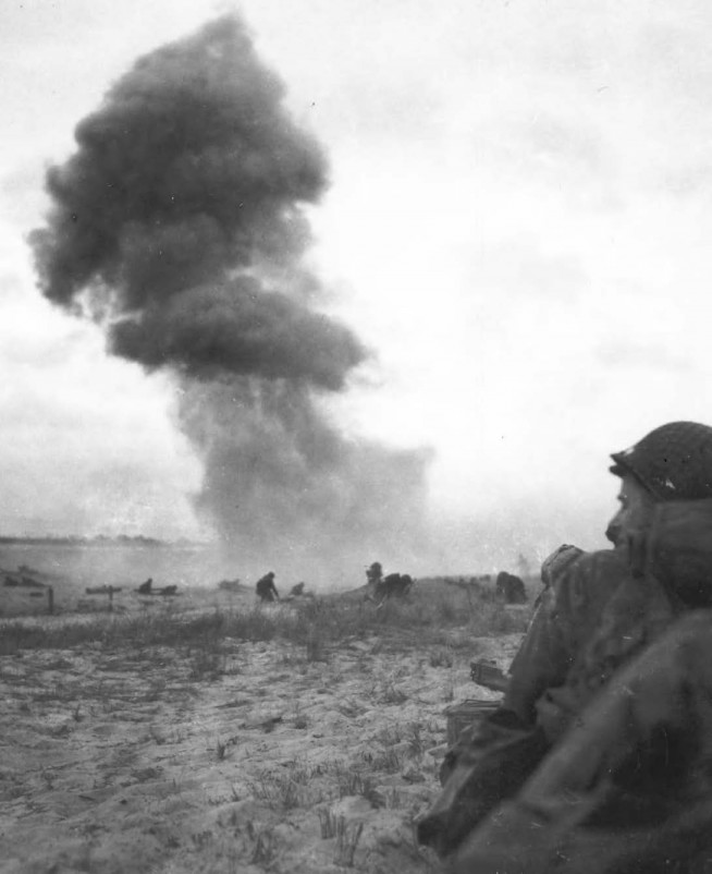 An enemy shell hits the beach where U. S. troops are advancing. Image and caption credit: Center of Military History, U.S. Army.