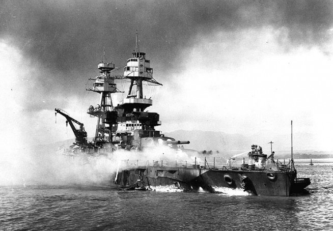 USS Nevada (BB-36) beached and burning after being hit forward by Japanese bombs and torpedoes. Her pilothouse area is discolored by fires in that vicinity. The harbor tug Hoga (YT-146) is alongside Nevada's port bow, helping to fight fires on the battleship's forecastle. Note channel marker bouy against Nevada's starboard side. Official U.S. Navy Photograph, National Archives Collection. Caption: Naval History & Heritage Command.