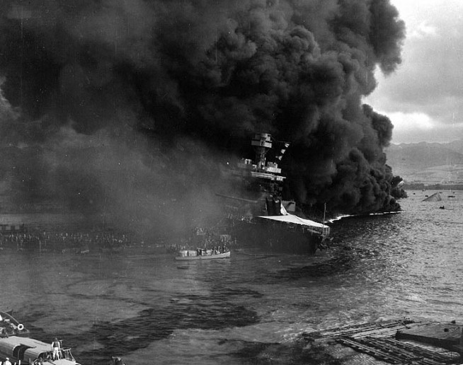 Crew abandoning the damaged USS California (BB-44) as burning oil drifts down on the ship, at about 1000 hrs on the morning of 7 December 1941, shortly after the end of the Japanese raid. The capsized hull of USS Oklahoma (BB-37) is visible at the right. Official U.S. Navy Photograph, NHHC Collection. Caption: Naval History & Heritage Command.
