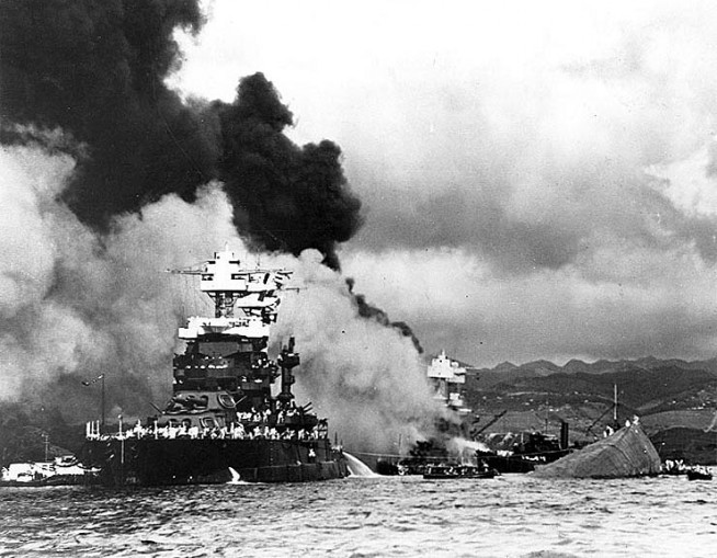 USS Maryland (BB-46) alongside the capsized USS Oklahoma (BB-37). USS West Virginia (BB-48) is burning in the background. Photo and caption: Naval History & Heritage Command.