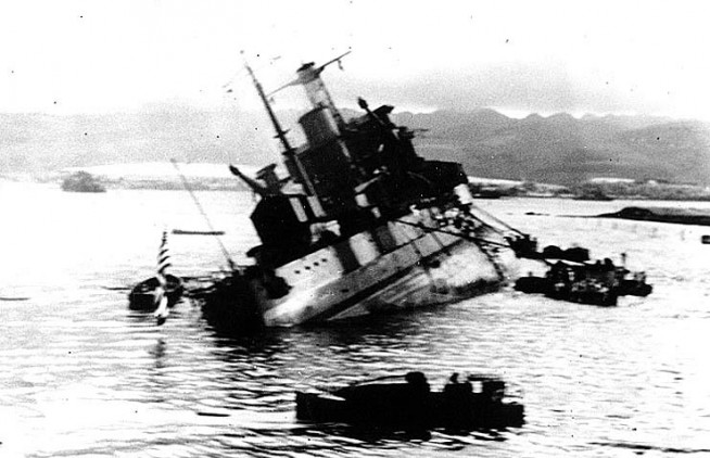 Capsizing off Ford Island, during the attack on Pearl Harbor, 7 December 1941, after being torpedoed by Japanese aircraft . Photographed from USS Tangier (AV-8), which was moored astern of Utah. Note colors half-raised over fantail, boats nearby, and sheds covering Utah's after guns. Official U.S. Navy Photograph, National Archives Collection. Caption: Naval History & Heritage Command.