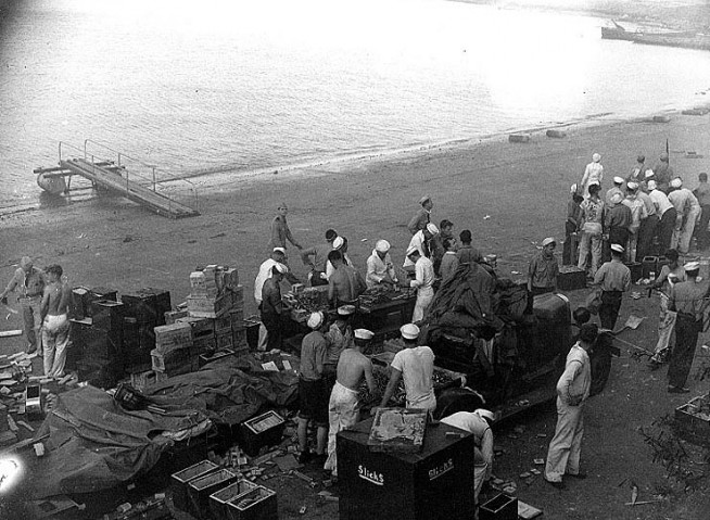 Sailors at Naval Air Station Ford Island reloading ammunition clips and belts, probably around the time of the attack's second wave. Note what appears to be a seaplane boarding gangway at top left, and beached motor launches in upper right. Also note variety of uniforms worn by those present. Official U.S. Navy Photograph, National Archives Collection. Caption: Naval History & Heritage Command.