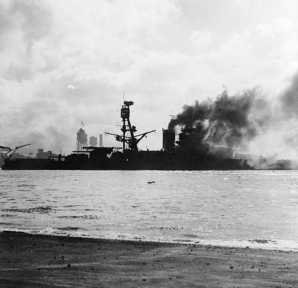 USS Nevada (BB-36) afire and down at the bow, after she was bombed by Japanese planes while attempting to get to sea. Photographed from Ford Island. Note men in Nevada's main top, manning .50 caliber machine guns. Official U.S. Navy Photograph, National Archives collection. Caption: Naval History & Heritage Command.