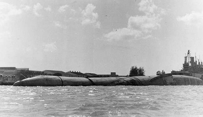 Capsized hull of USS Utah (AG-16) off the western side of Ford Island on 12 December 1941, five days after she was sunk by Japanese aerial torpedoes during the Pearl Harbor Attack. View looks toward Ford Island, with Utah's bow at left. USS Tangier (AV-8) is in the right background. Collection of Vice Admiral Homer N. Wallin. NHHC Photograph. Caption: Naval History & Heritage Command.