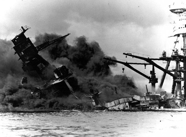 The forward superstructure and midships gun positions of the sunken USS Arizona (BB-39), afire after the Japanese raid, 7 December 1941. At right are the ship's mainmast and boat cranes, which were beyond the areas wrecked by the explosion of her forward magazines. Official U.S. Navy Photograph, NHHC collection. Caption: Naval History & Heritage Command.