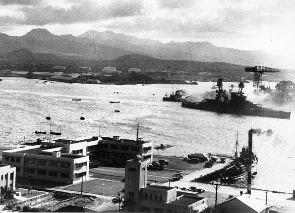 USS Nevada (BB-36) headed down channel past the Navy Yard's 1010 Dock, under Japanese air attack during her sortie from "Battleship Row". A camouflage Measure 5 false bow wave is faintly visible painted on the battleship's forward hull. Photographed from Ford Island. Small ship in the lower right is USS Avocet (AVP-4). Note fuel tank "farm" in the left center distance, beyond the Submarine Base. Official U.S. Navy Photograph, NHHC Collection. Caption: Naval History & Heritage Command.