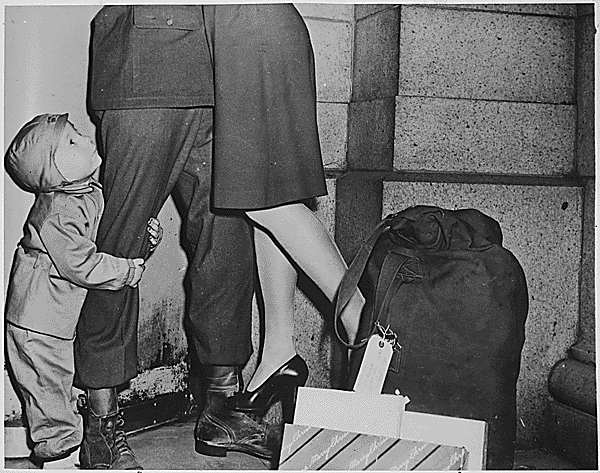 A youngster, clutching his soldier father (home for Christmas), as his father lifts his wife from the ground 12/1944. Credit: National Archives.
