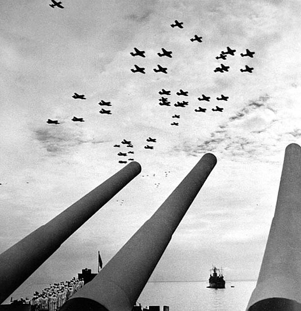 U.S. Navy carrier planes fly in formation over USS Missouri (BB-63) during the surrender ceremonies, 2 September 1945. Photographed by Lieutenant Barrett Gallagher, USNR, from atop Missouri's forward 16-inch gun turret. Aircraft types include F4U, TBM and SB2C. Ship in the right distance is USS Ancon (AGC-4). Credit: Naval Historical Center.
