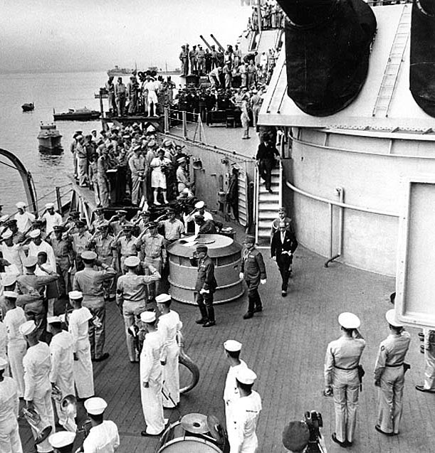 The Japanese delegation receives honors as they depart USS Missouri (BB-63) at the conclusion of the surrender ceremonies, 2 September 1945. General Yoshijiro Umezu is in the center, saluting. Photographed by Lieutenant Barrett Gallagher, USNR, from atop Missouri's forward 16-inch gun turret. Note photographers on platforms in the background, band in the lower left and "seahorse" insignia on the shoulder by the Marine in lower right. Credit: Naval Historical Center.