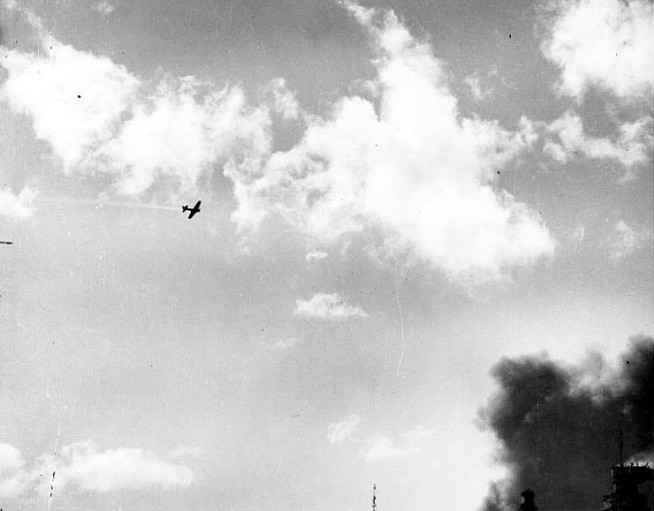Japanese Type 00 Carrier Fighter ("Zero") trailing smoke after it was hit by anti-aircraft fire during the attack. The masthead machinegun platform of a battleship is visible in the lower right. Official U.S. Navy Photograph, now in the collections of the National Archives. Caption: Naval History & Heritage Command.