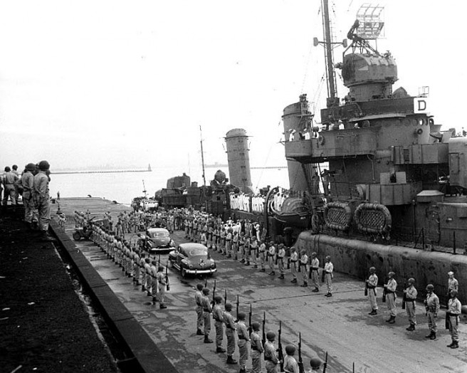 A U.S. Army honor guard presents arms as representatives of the Allied Powers arrive at pierside to be taken to USS Missouri for the surrender ceremonies, 2 September 1945. Uniform patches and unit flag indicate that the honor guard is from the 11th Airborne Division Reconnaissance Battalion. USS Buchanan (DD-484) is alongside the pier. She carried some of the dignitaries out to the Missouri. Credit: Naval Historical Center.