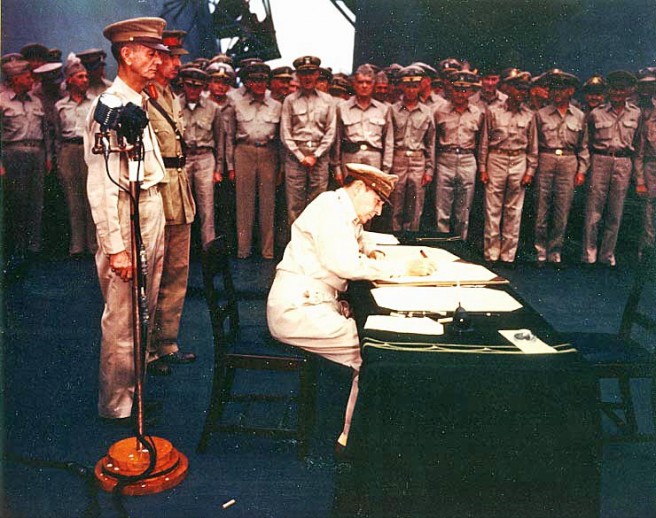 General of the Army Douglas MacArthur signs the Instrument of Surrender, as Supreme Allied Commander, on board USS Missouri (BB-63), 2 September 1945. Behind him are Lieutenant General Jonathan M. Wainwright, U.S. Army, and Lieutenant General Sir Arthur E. Percival, British Army, both of whom had just been released from Japanese prison camps. Credit: Naval Historical Center.