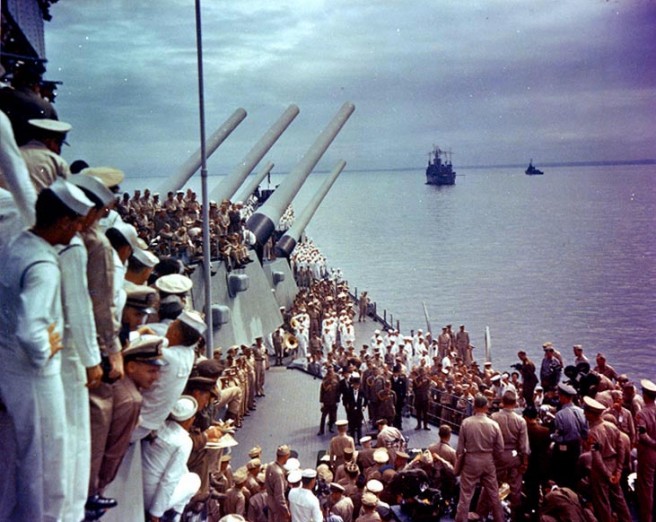 View of the surrender ceremonies, looking forward from USS Missouri's superstructure, as Admiral Conrad E.L. Helfrich signs the Instrument of Surrender on behalf of The Netherlands. General of the Army Douglas MacArthur is standing beside him. Credit: Naval Historical Center.