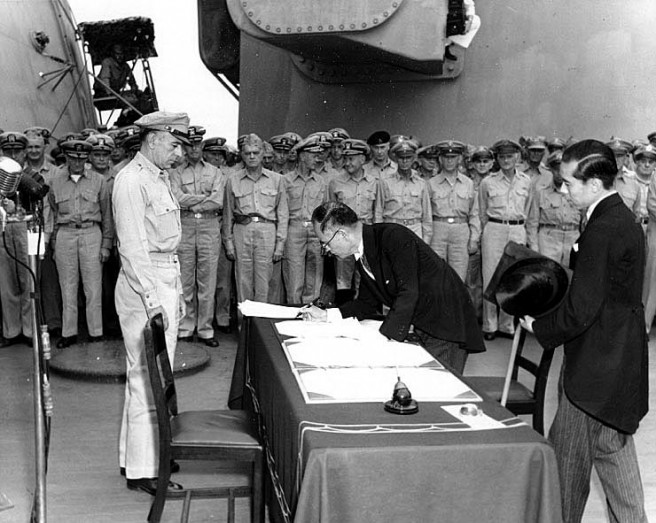 Japanese Foreign Minister Mamoru Shigemitsu signs the Instrument of Surrender on behalf of the Japanese Government, on board USS Missouri (BB-63), 2 September 1945. Lieutentant General Richard K. Sutherland, U.S. Army, watches from the opposite side of the table. Foreign Ministry representative Toshikazu Kase is assisting Mr. Shigemitsu. Credit: Naval Historical Center.