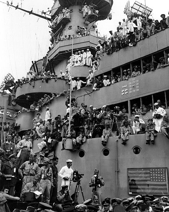 Spectators and photographers crowd USS Missouri's superstructure to witness the formal ceremonies marking Japan's surrender, 2 September 1945. The framed flag in lower right is that hoisted by Commodore Matthew C. Perry on 14 July 1853, in Yedo (Tokyo) Bay, on his first expedition to negotiate the opening of Japan. It had been brought from its permanent home in Memorial Hall at the U.S. Naval Academy for use during the surrender ceremonies. Credit: Naval Historical Center.