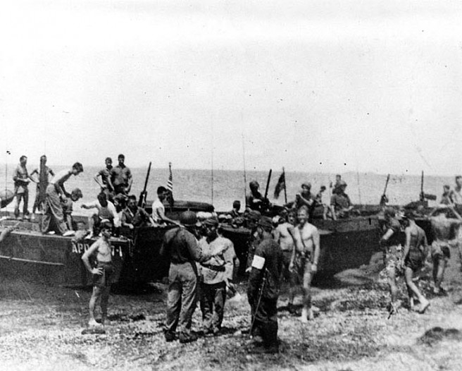 Lieutenant Commander Edward Porter Clayton, USN, (center, back to camera) Commanding Officer of Underwater Demolition Team 21, receiving the first sword surrendered to an American force in the Japanese Home islands. The surrender was made by a Japanese Army Coast Artillery Major (standing opposite LCdr. Clayton) at Futtsu-misaki, across Tokyo Bay from Yokosuka Navy Base on 28 August 1945. Members of UDT-21 had landed from USS Burke (APD-65), whose boats are beached in this view. Credit: Naval Historical Center.