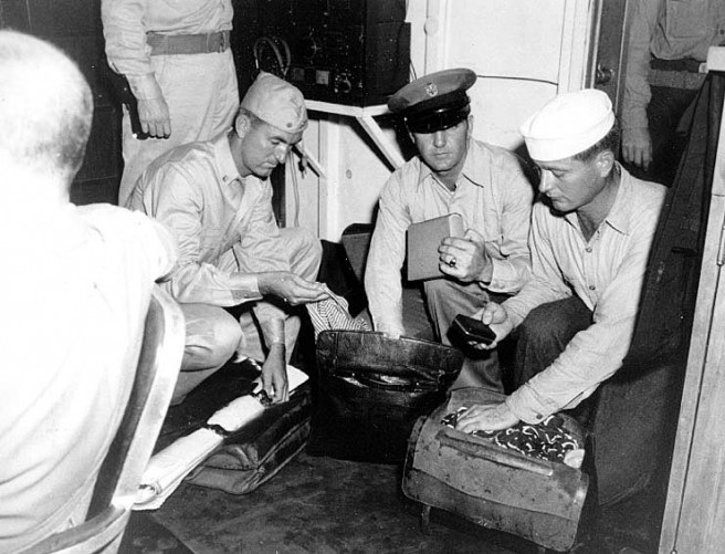 Japanese officers' briefcases are searched for possible weapons, in the wardroom of USS Nicholas (DD-449), as the destroyer carried them to confer with Allied representatives concerning the entry of U.S. and British warships into Sagami Wan and Tokyo Bay, 27 August 1945. Nicholas's Executive Officer, Lieutenant Commander Raynha Townshend, USNR, is in the left center. Credit: Naval Historical Center.
