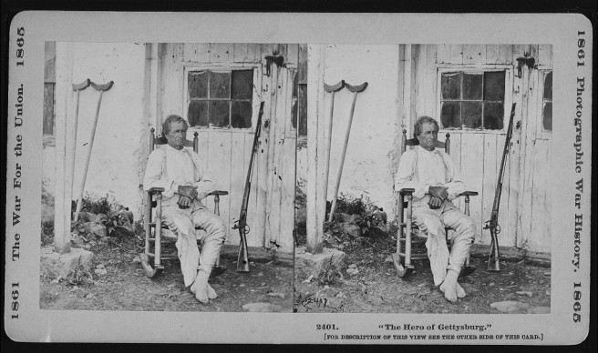 War veteran John Burns seated outside in a rocking chair with his musket propped near the door to a building, ca 1861-1865. Credit: Library of Congress.