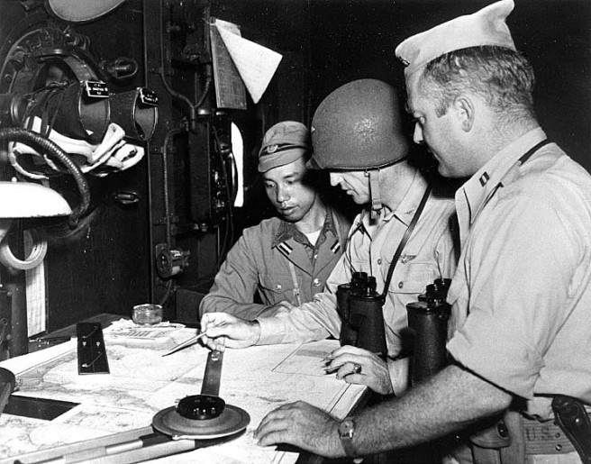 USS Cumberland Sound (AV-17) Ship's Commanding Officer, Captain Etheridge Grant, USN, (center), checks charts with a Japanese Navy pilot and Lieutenant Rogers, USN, (at right), as the seaplane tender prepares to enter Tokyo Bay, 28 August 1945. Credit: Naval Historical Center