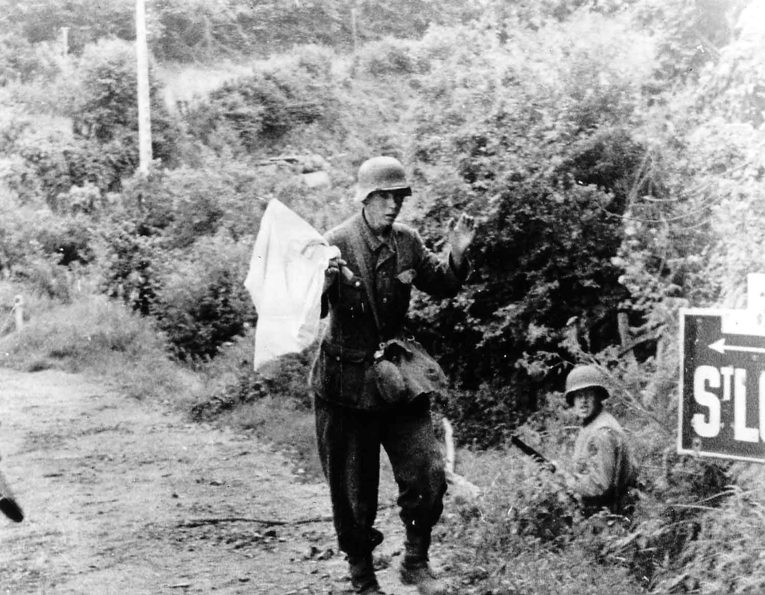 German soldier carrying a white flag surrenders to American troops on the outskirts of St-Lo. Ca. 18-20 July 1944. Public Domain.